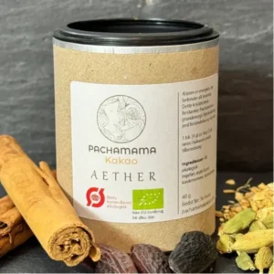 Kraft paper jar labeled Pachamama Kakao Aether cacao with cinnamon sticks and assorted spices beside it on a dark surface