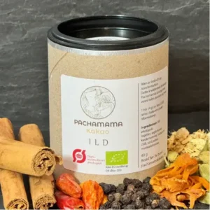 Kraft paper canister with a black lid labeled Pachamama cacao 1LD, set on a dark background, surrounded by cinnamon sticks and dried spices (orange peels, red chilies, and dark cacao nibs).