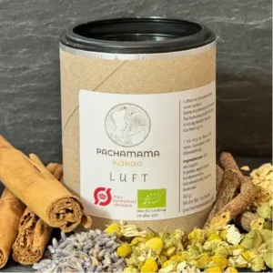 Tin of Pachamama Kakao Luft cocoa powder with a white label, flanked by cinnamon sticks and dried flowers on a dark background.