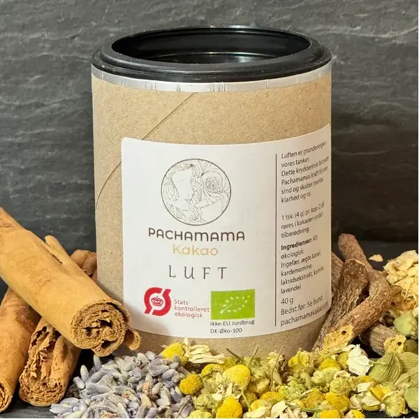 Tin of Pachamama Kakao Luft cocoa powder with a white label, flanked by cinnamon sticks and dried flowers on a dark background.