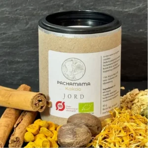 Cylindrical kraft tin of Pachamama Kakao Jord on a dark surface, with a white label and cinnamon sticks nearby.
