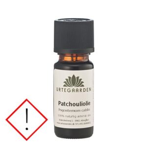 Dark amber bottle of Urtegaarden Patchouli oil with a black cap, placed beside a red-outlined warning diamond with an exclamation mark.